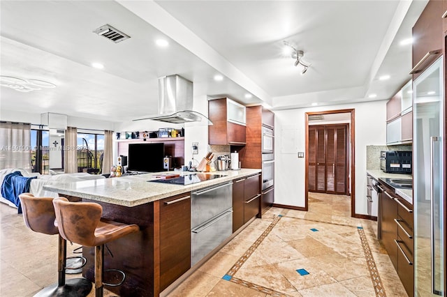 kitchen with kitchen peninsula, tasteful backsplash, range hood, and a breakfast bar area