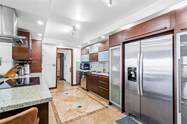 kitchen with wall chimney range hood, appliances with stainless steel finishes, light stone countertops, sink, and decorative backsplash