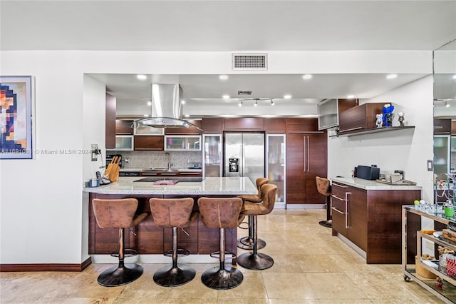 kitchen with island exhaust hood, stainless steel refrigerator with ice dispenser, sink, a breakfast bar, and kitchen peninsula