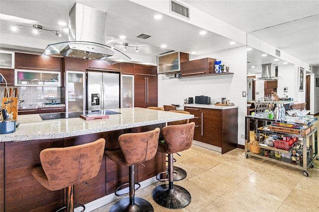 kitchen featuring light stone counters, black electric stovetop, island exhaust hood, and stainless steel fridge