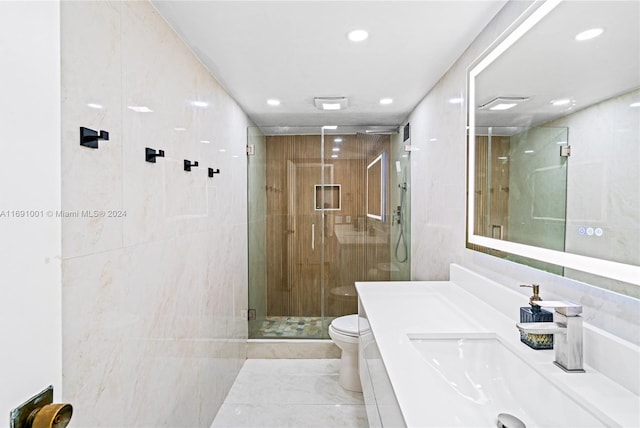 bathroom with tile walls, vanity, toilet, and a shower with shower door