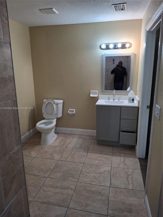 bathroom with tile patterned flooring, vanity, toilet, and a textured ceiling