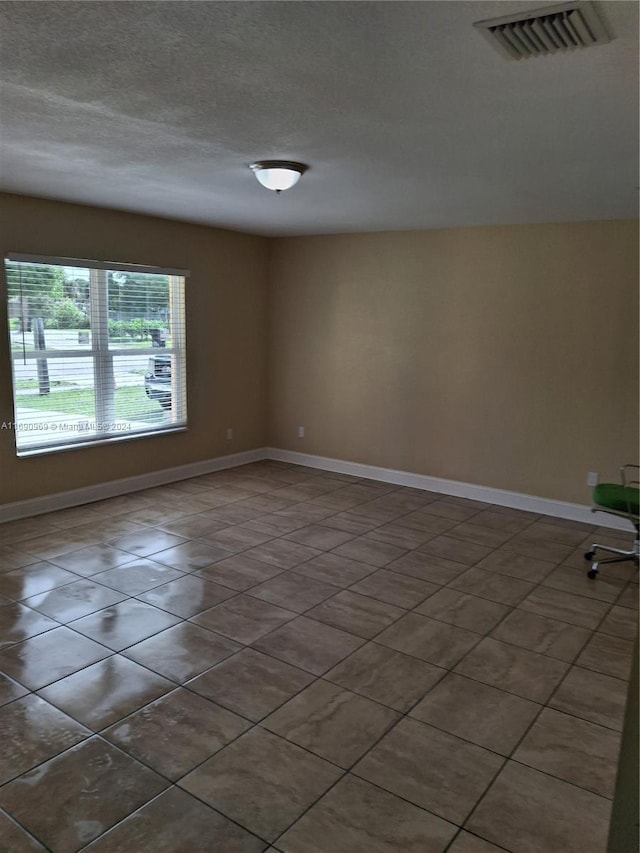 spare room featuring dark tile patterned flooring and a textured ceiling