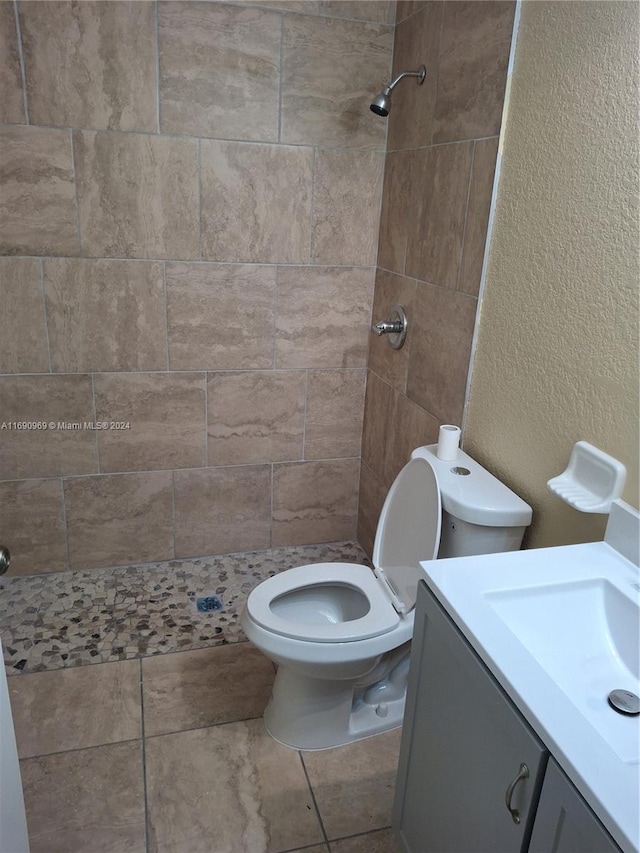 bathroom featuring toilet, tile patterned flooring, vanity, and a tile shower