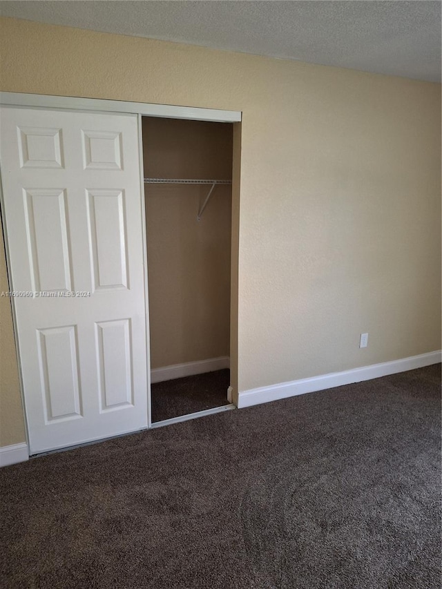 unfurnished bedroom featuring a closet, a textured ceiling, and dark carpet