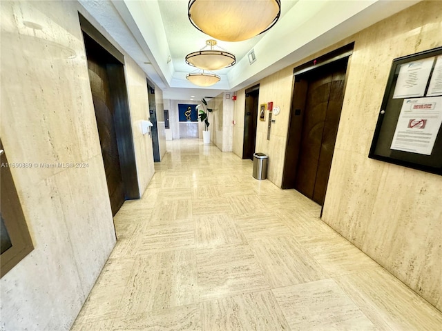 hallway with elevator and a tray ceiling