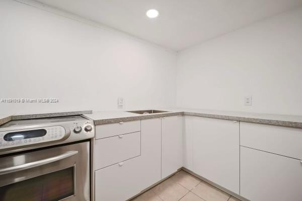 kitchen featuring stainless steel electric range, light tile patterned floors, and white cabinets