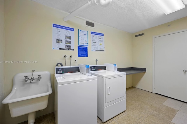 clothes washing area with a textured ceiling, sink, and washer and clothes dryer