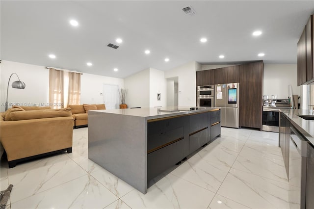 kitchen with a large island with sink, appliances with stainless steel finishes, and dark brown cabinets