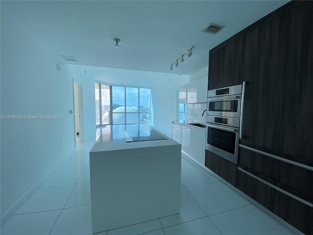 kitchen with white cabinetry, light tile patterned floors, black electric cooktop, double oven, and a center island