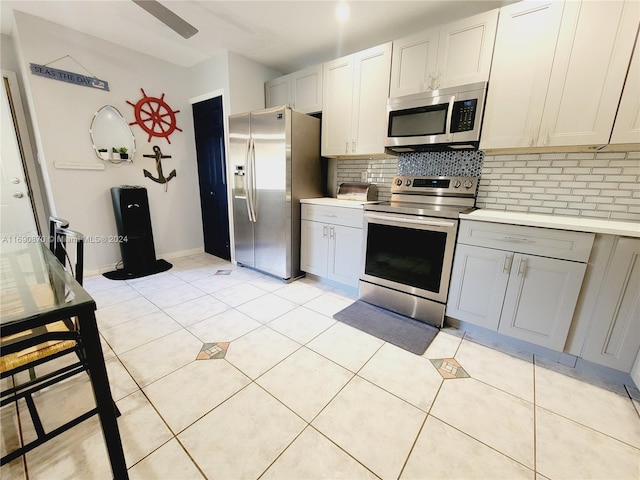 kitchen with tasteful backsplash, gray cabinets, light tile patterned floors, and appliances with stainless steel finishes