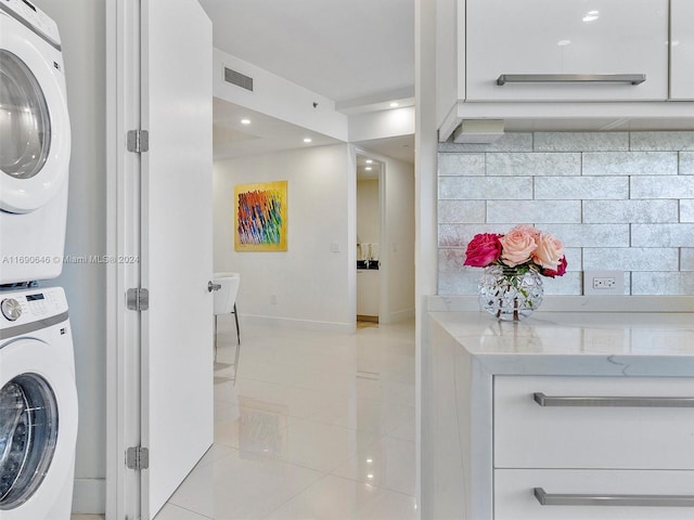 clothes washing area featuring stacked washing maching and dryer and light tile patterned floors