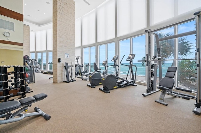 exercise room with a towering ceiling, a water view, and floor to ceiling windows