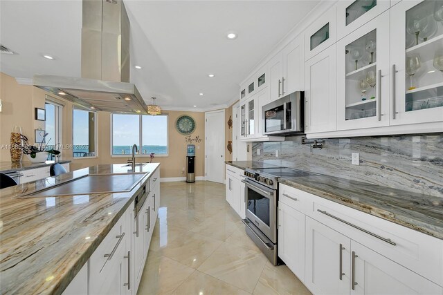 kitchen with tasteful backsplash, island exhaust hood, white cabinetry, premium appliances, and dark stone countertops