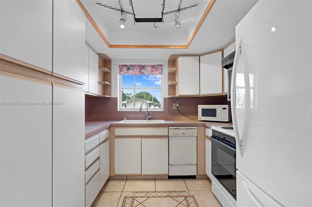 kitchen with white appliances, a raised ceiling, sink, white cabinets, and light tile patterned flooring