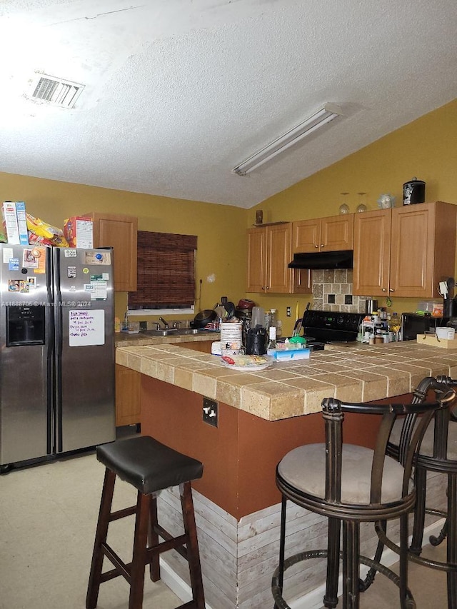 kitchen featuring stainless steel fridge with ice dispenser, a textured ceiling, black range oven, and a breakfast bar