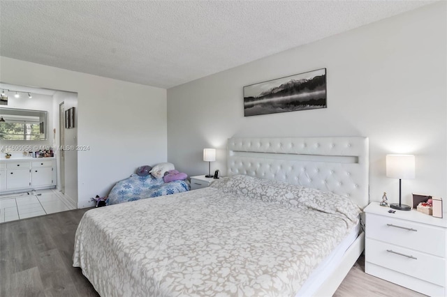 bedroom with ensuite bathroom, a textured ceiling, and light hardwood / wood-style flooring