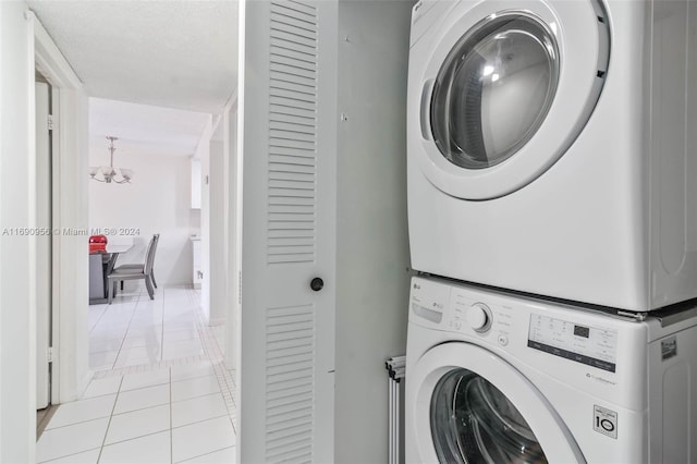 laundry room featuring a textured ceiling, light tile patterned floors, stacked washer / dryer, and an inviting chandelier