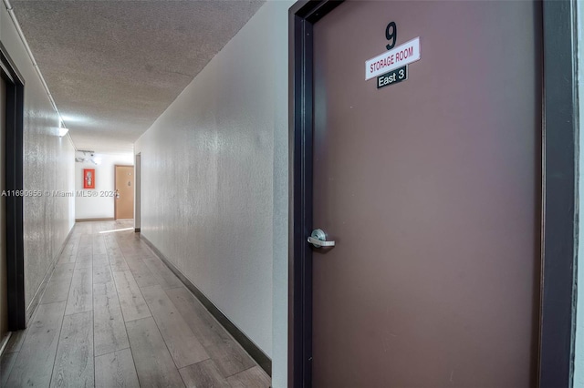 corridor with a textured ceiling and light hardwood / wood-style flooring