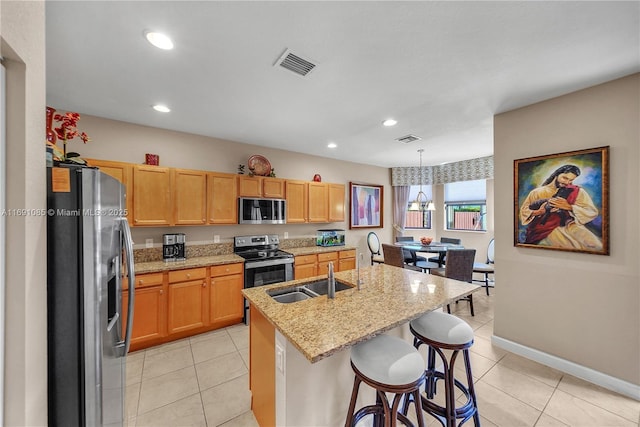 kitchen featuring sink, a center island with sink, pendant lighting, stainless steel appliances, and light stone countertops