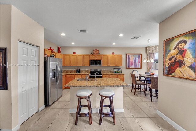 kitchen with a breakfast bar, pendant lighting, stainless steel appliances, light stone countertops, and a kitchen island with sink