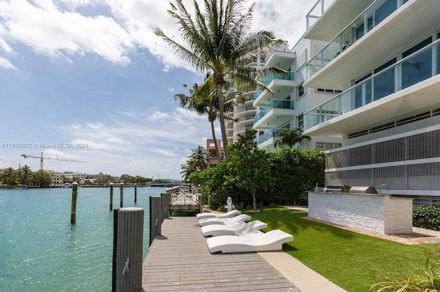 view of dock with a water view, a lawn, and a balcony