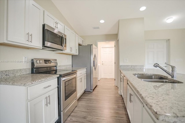 kitchen with white cabinets, sink, appliances with stainless steel finishes, light hardwood / wood-style floors, and light stone counters