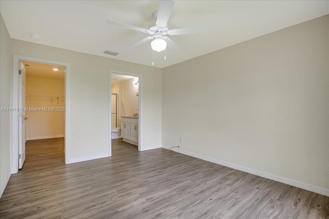 unfurnished bedroom featuring ensuite bath, a spacious closet, ceiling fan, light hardwood / wood-style floors, and a closet