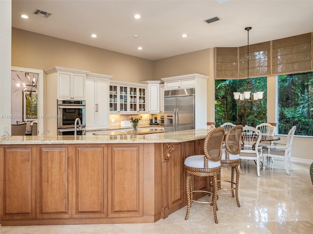 kitchen with appliances with stainless steel finishes, light stone countertops, hanging light fixtures, decorative backsplash, and a chandelier