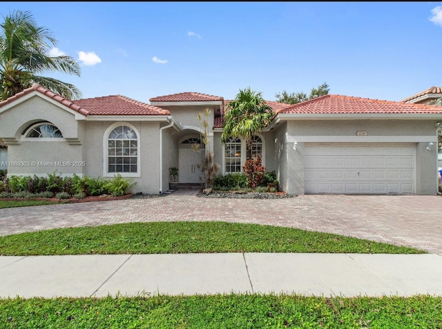 mediterranean / spanish-style house featuring stucco siding, decorative driveway, a garage, and a tile roof