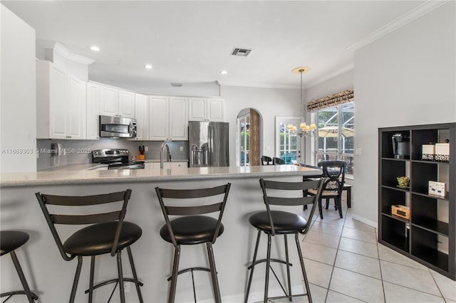kitchen featuring appliances with stainless steel finishes, a chandelier, a peninsula, white cabinetry, and light tile patterned floors
