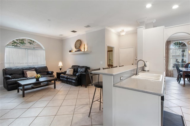 kitchen with a sink, light tile patterned floors, light countertops, a breakfast bar, and crown molding