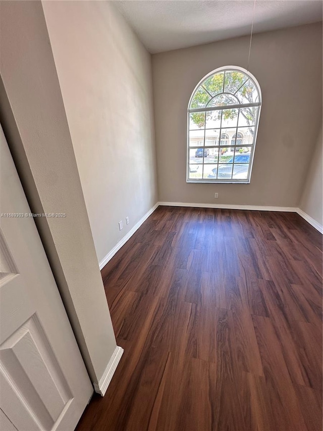spare room featuring dark wood-type flooring and baseboards