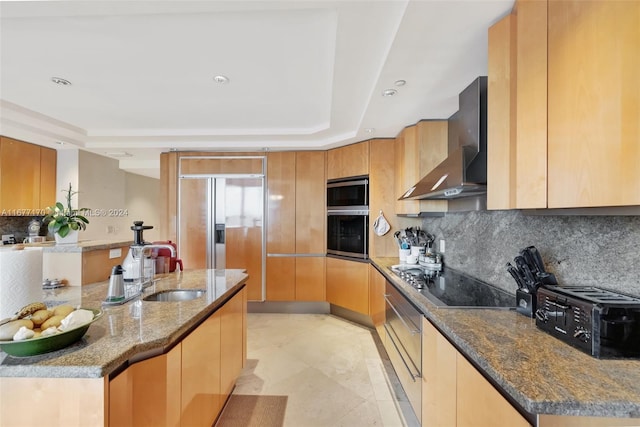 kitchen with stone countertops, black appliances, a raised ceiling, wall chimney range hood, and backsplash