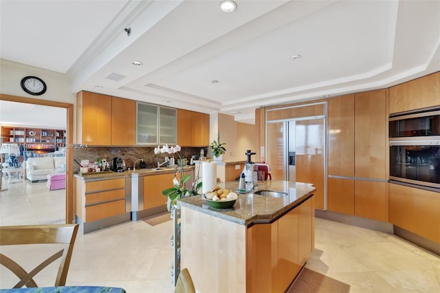 kitchen with sink, appliances with stainless steel finishes, light stone countertops, a tray ceiling, and decorative backsplash