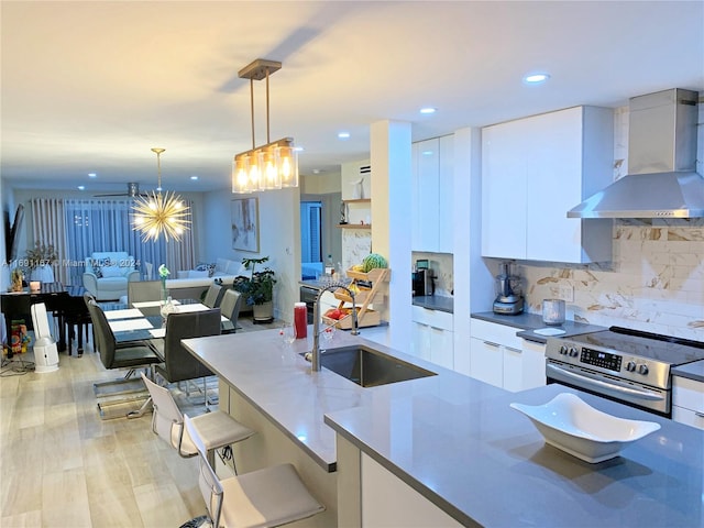 kitchen featuring stainless steel electric range oven, wall chimney range hood, decorative light fixtures, light hardwood / wood-style floors, and white cabinetry