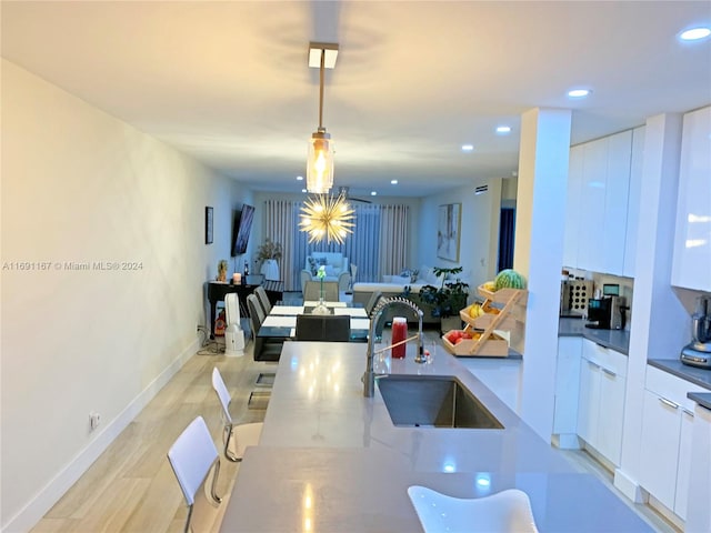 kitchen with light stone countertops, decorative light fixtures, white cabinetry, and sink