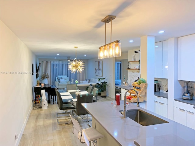 kitchen with pendant lighting, white cabinets, sink, light hardwood / wood-style flooring, and light stone countertops