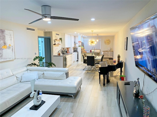 living room with wine cooler, ceiling fan with notable chandelier, and light hardwood / wood-style flooring