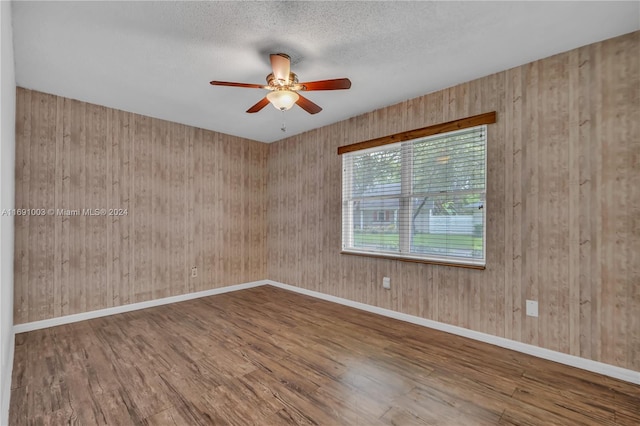 spare room featuring wood walls, a textured ceiling, hardwood / wood-style flooring, and ceiling fan