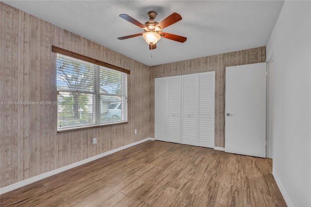 unfurnished bedroom with a closet, a textured ceiling, wood walls, light hardwood / wood-style floors, and ceiling fan