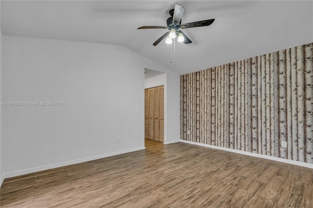 empty room featuring wood walls, wood-type flooring, and vaulted ceiling