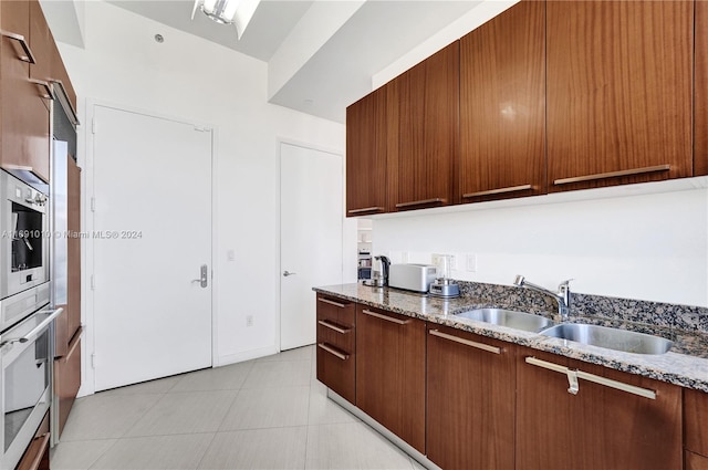 kitchen with dark stone countertops, sink, oven, and light tile patterned floors