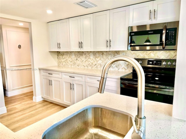 kitchen with backsplash, appliances with stainless steel finishes, light stone countertops, light hardwood / wood-style floors, and white cabinets