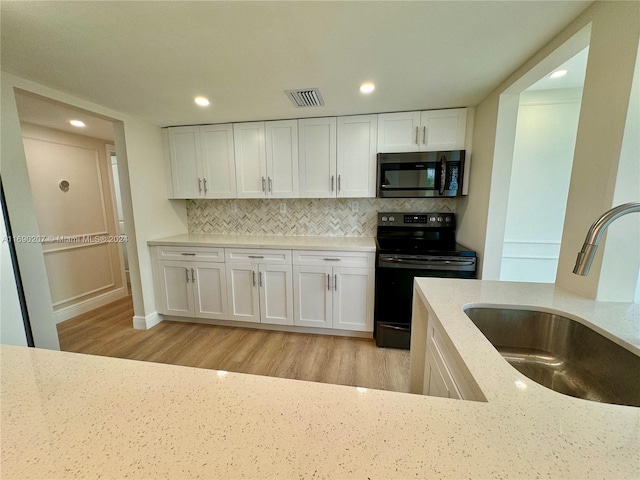 kitchen with white cabinets, sink, electric range, light stone countertops, and light wood-type flooring