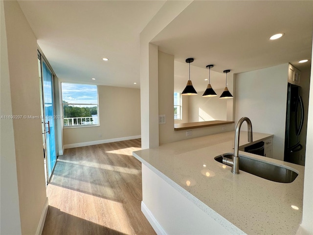 kitchen featuring light hardwood / wood-style floors, black fridge, sink, light stone countertops, and decorative light fixtures