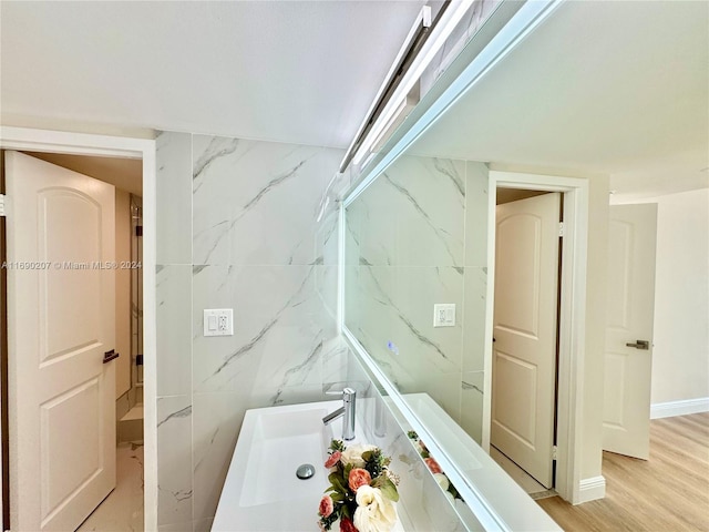 bathroom with tile walls, wood-type flooring, sink, and a tub