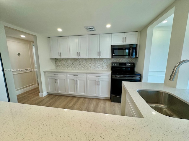16546 NE 26th Ave Unit 3G, North Miami Beach, FL 33160 - kitchen with electric range, white cabinetry, light wood-type flooring, backsplash, and recessed lighting