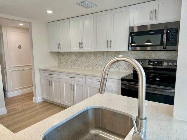 16546 NE 26th Ave Unit 3G, North Miami Beach, FL 33160 - kitchen featuring stainless steel microwave, black electric range oven, white cabinets, decorative backsplash, and recessed lighting