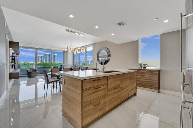 kitchen featuring expansive windows, pendant lighting, sink, and a kitchen island with sink